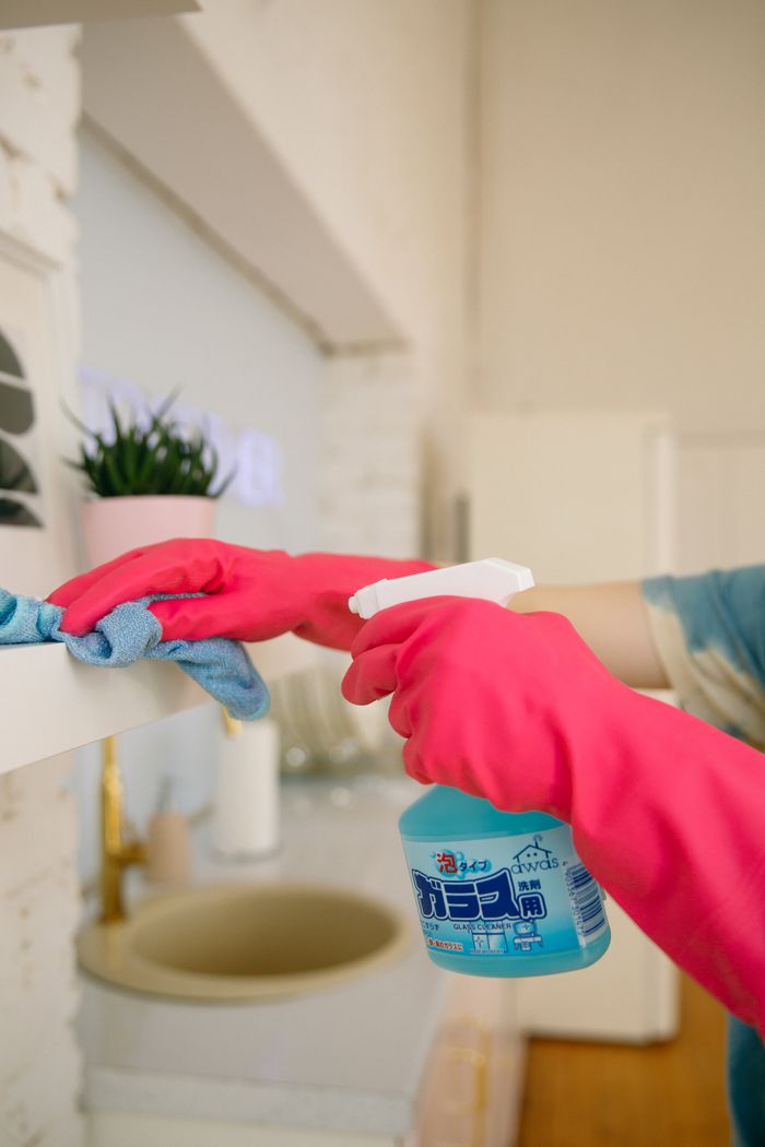 Une personne utilisant un vaporisateur et un chiffon pour nettoyer une étagère de cuisine, afin de garantir hygiène et propreté.